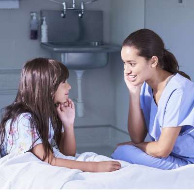 Nurse talking with girl patient sitting up in bed on hospital children's ward