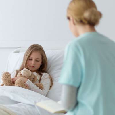 Young woman rading a book to sick little girl lying in a hospital bed