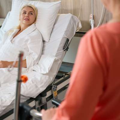 Woman in a hospital gown sits on a special bed, next to a nurse with a wheelchair